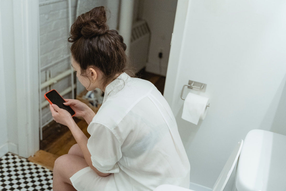 Woman seated on a toilet looking at her smartphone.