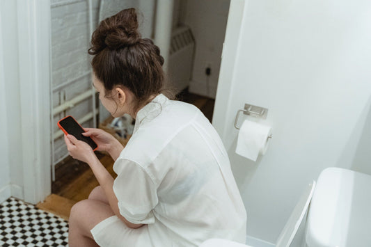 Woman seated on a toilet looking at her smartphone.